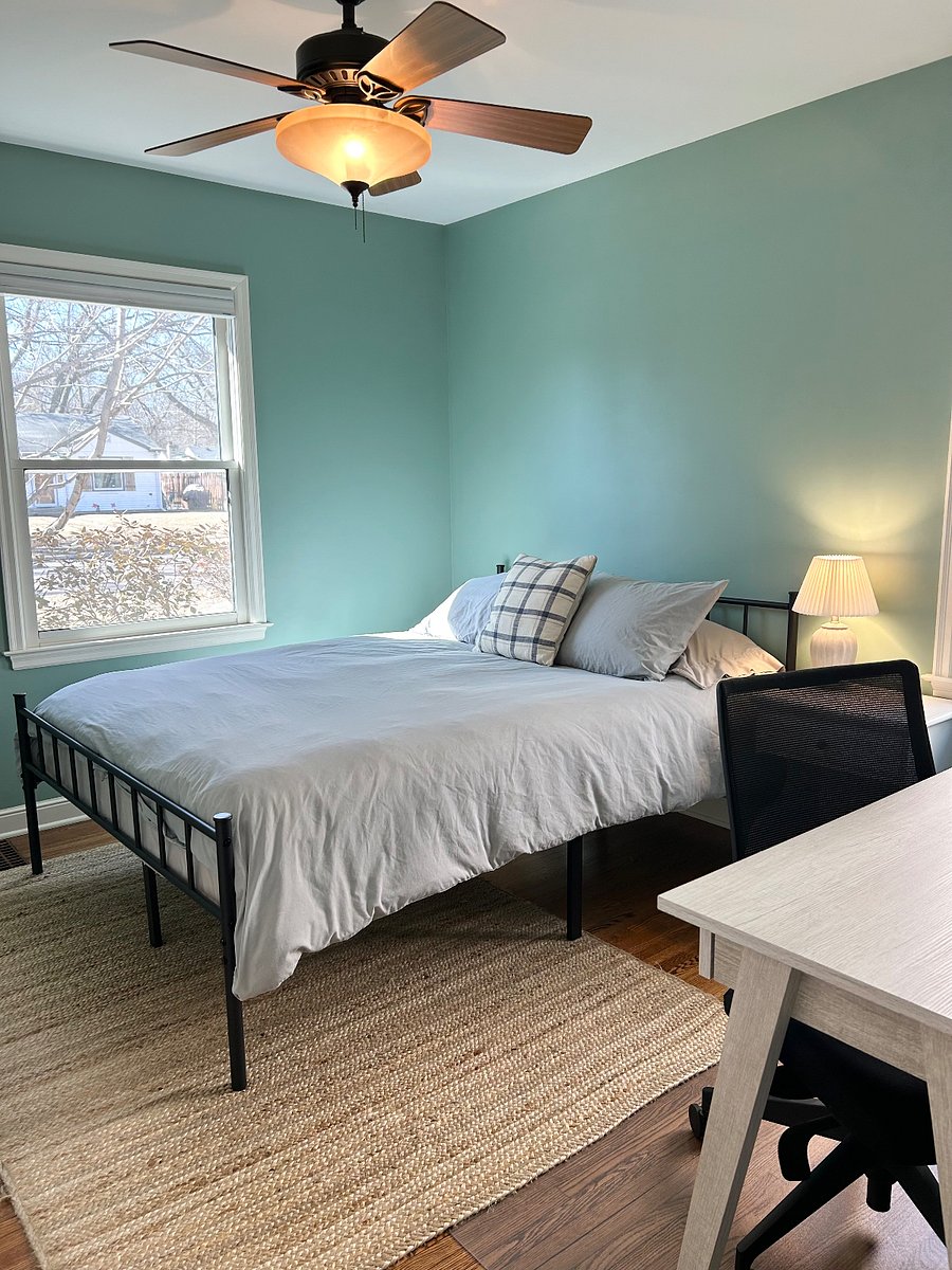 Main floor bedroom 2 features a queen size bed, desk and chair, nightstand, lamp, closet with a laundry basket and hangers.