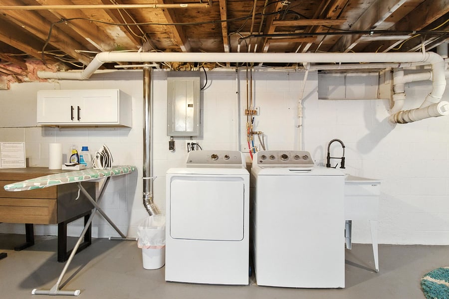 The unfinished basement has a washer and dryer, iron/board, and a starter supply of laundry products.