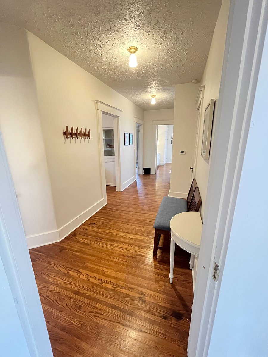 view down the hallway with landing bench and table on right and coat/purse pegs on left