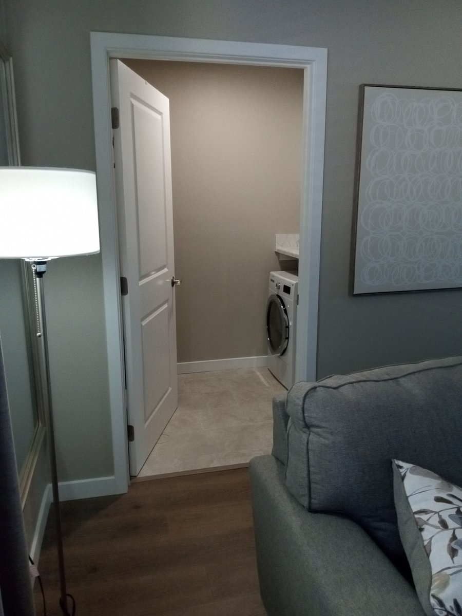 Inside private laundry room with laundry basket, washer/dryer, folding table, iron and ironing board as well as swifter, broom/ pan and small ladder.