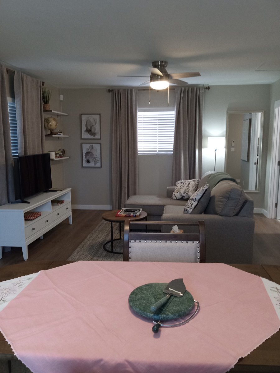 Living room with black out drapes, Smart TV, standing lamp, full length mirror between curtains and laundry room, book shelves and TV table with drawers and shelves.