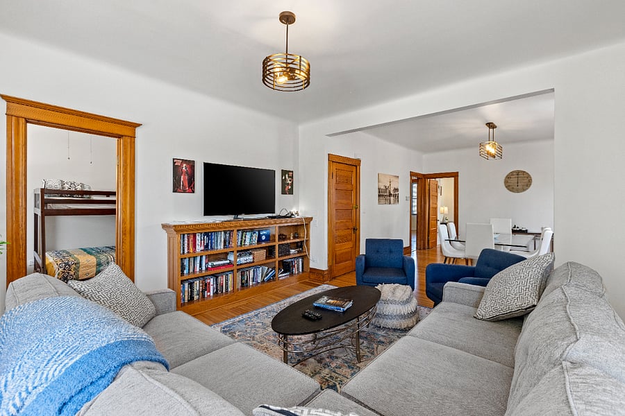 This spacious living room offers ample seating for both lively gatherings or a peaceful, much-needed nap. Enjoy entertainment with a Smart TV, DVD player, an array of DVDs, and a thoughtfully curated library of books. Lush plants bring a touch of nature indoors, while an antique heirloom kidney-shaped desk creates a charming workstation in the turret, tucked elegantly in the corner.