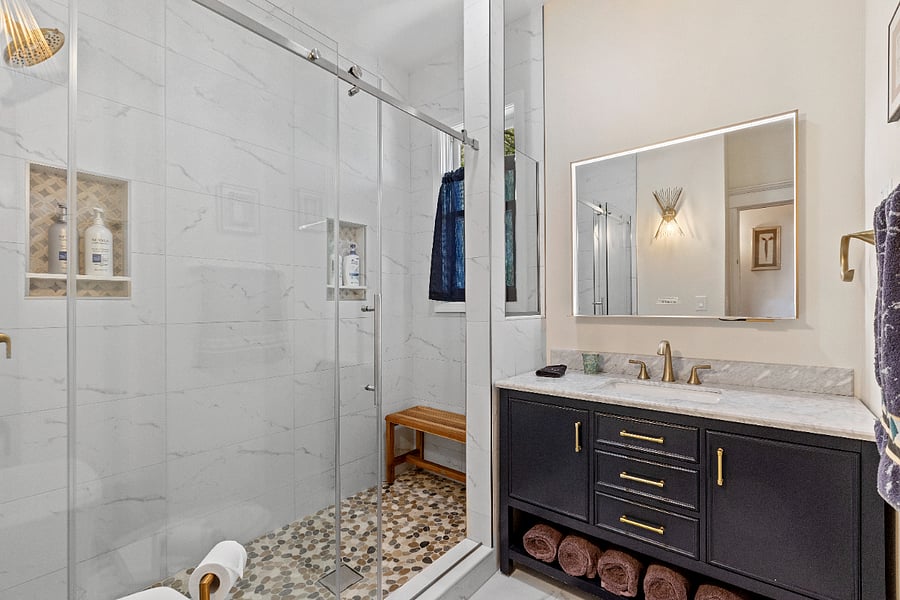 Indulge in the spa-like ambiance of this luxurious bathroom, featuring a stunning seven-foot stone walk-in shower complete with a teak bench for ultimate relaxation. The mirror is equipped with Wi-Fi speakers, allowing you to serenade yourself with your favorite tunes while you unwind in the shower.