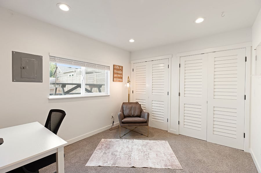 Office space in located in detached garage. It includes a chair, desk, lamp and a wide screen monitor.