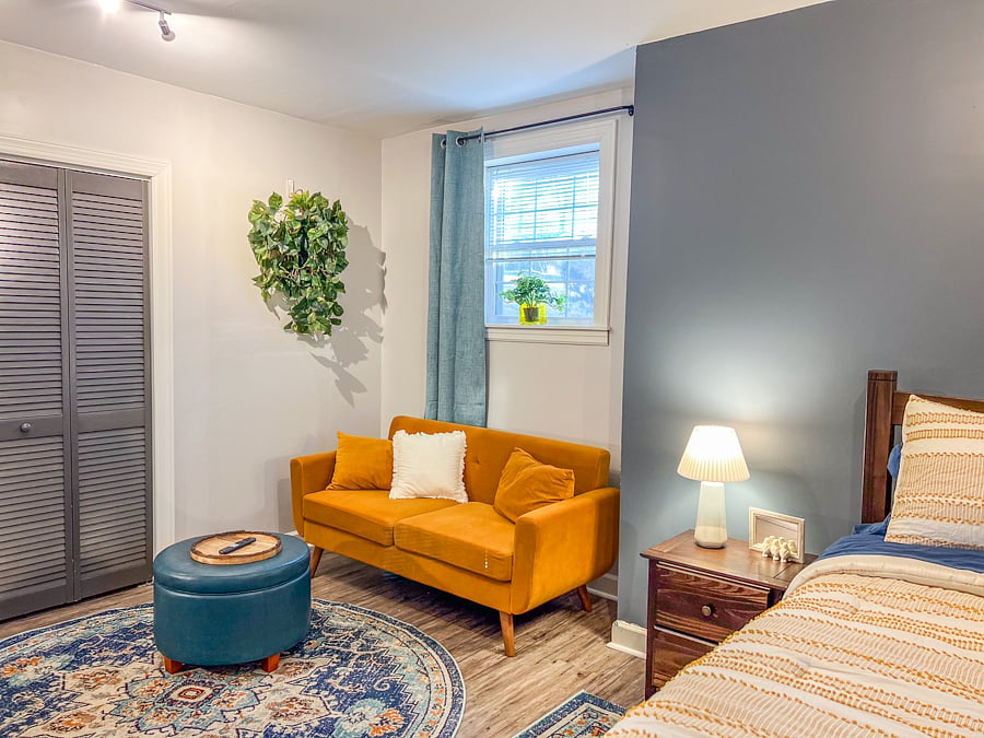 Large bedroom with wall-mounted smart tv, couch, ottoman, work desk and chair.