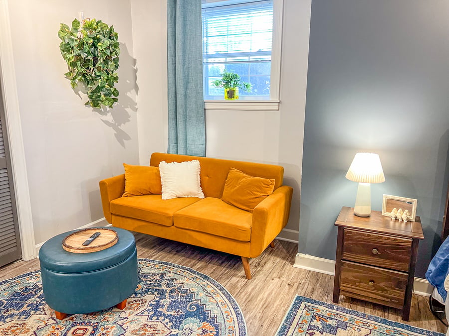 Large bedroom with wall-mounted smart tv, couch, ottoman, work desk and chair.