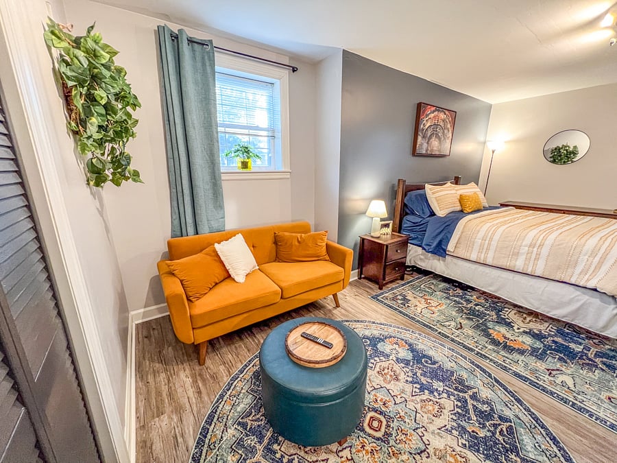 Large bedroom with wall-mounted smart tv, couch, ottoman, work desk and chair.