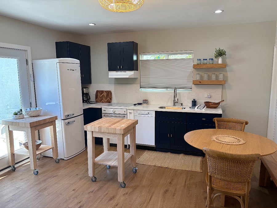 delightful kitchen with navy blue cabinets, wood floating shelves, white quartzite counters and backsplash, classic retro fridge, and induction stove/oven
