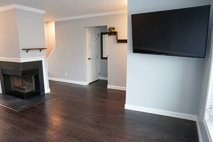 main floor living room, hardwood flooring, large bay window, wood burning fireplace; across the room is the door leading to the downstairs laundry room and walkout