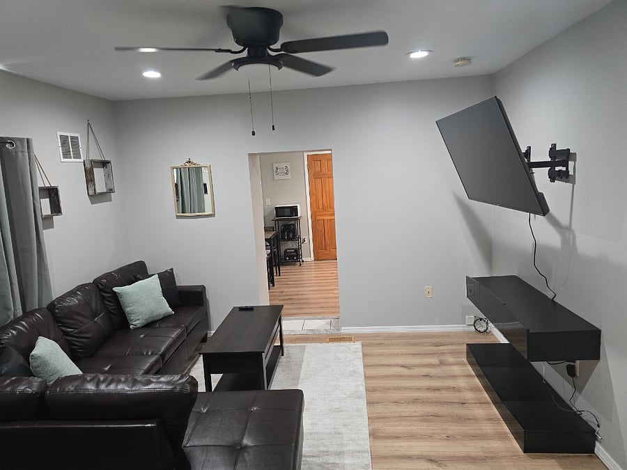 Living room area with large sectional couch, coffee table, large smart TV on wall and doorway into kitchen