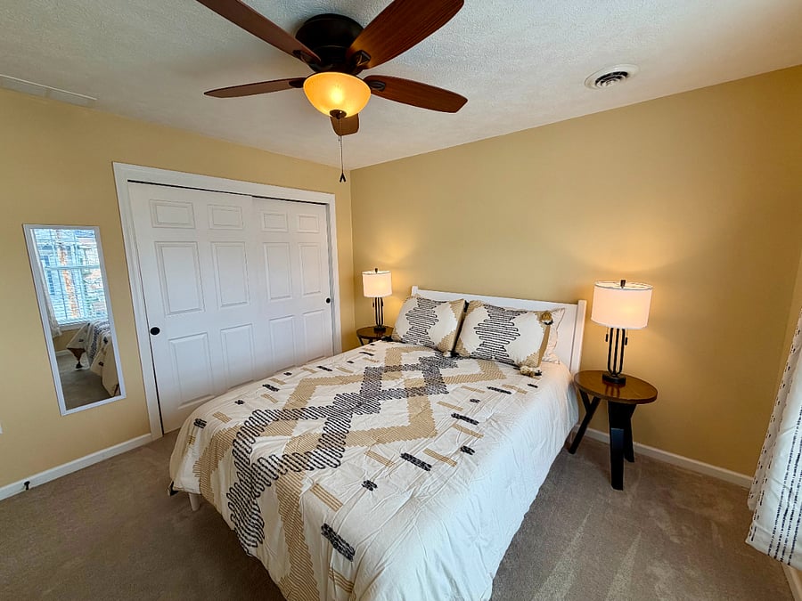 The secondary bedroom has a queen bed, closet, night stands with lamps, and adjustable sit/stand desk and chair.