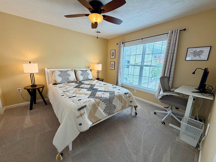 The secondary bedroom has a queen bed, closet, night stands with lamps, and adjustable sit/stand desk and chair.