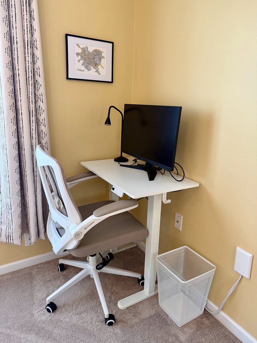 The secondary bedroom offers a dedicated area for a desk setup, including a small adjustable sit/stand desk, desk chair, monitor, task lamp, and waste basket - perfect for work, study, or hobbies.