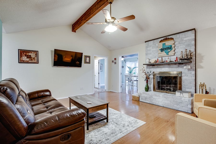 Living room has a couch and loveseat, with vaulted ceiling, ceiling fan, 55" smart TV, and wood fireplace