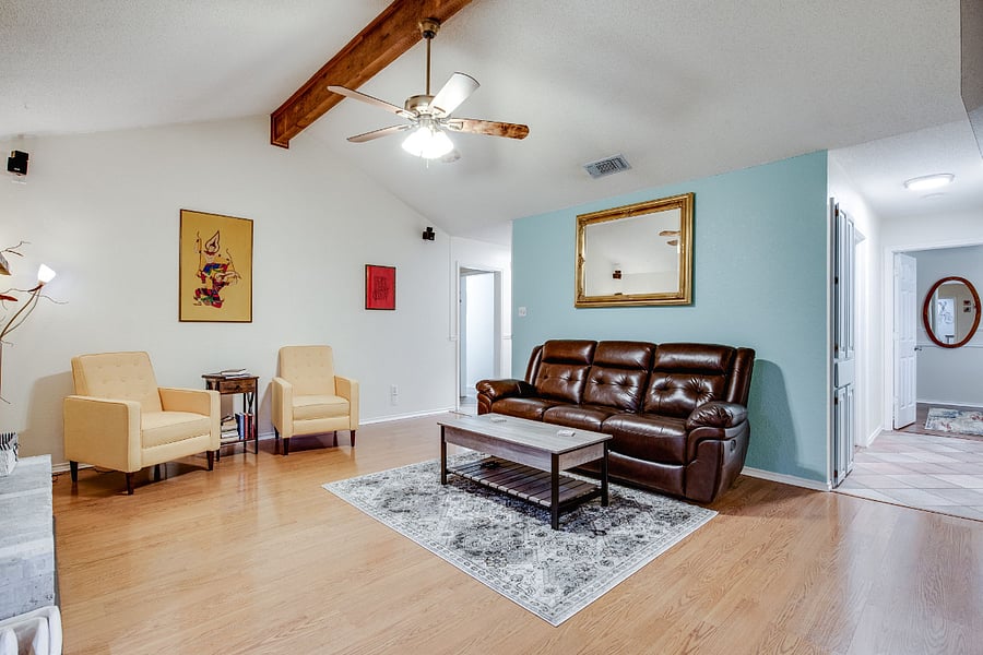Living room has a couch and loveseat, with vaulted ceiling, ceiling fan, 55" smart TV, and wood fireplace