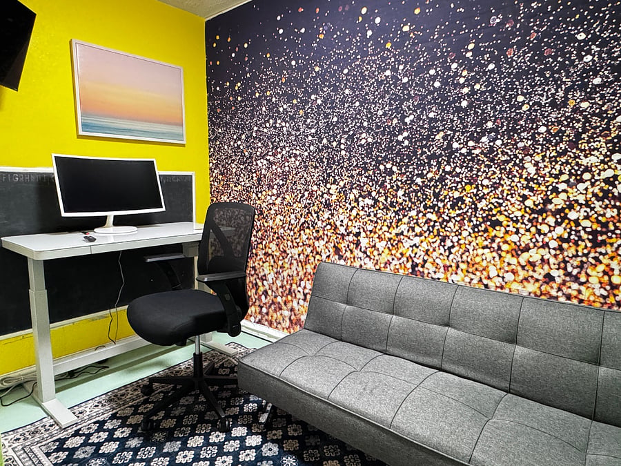 Private office with 27" curved monitor, smart TV, couch, and electronically adjustable desk for sitting or standing.