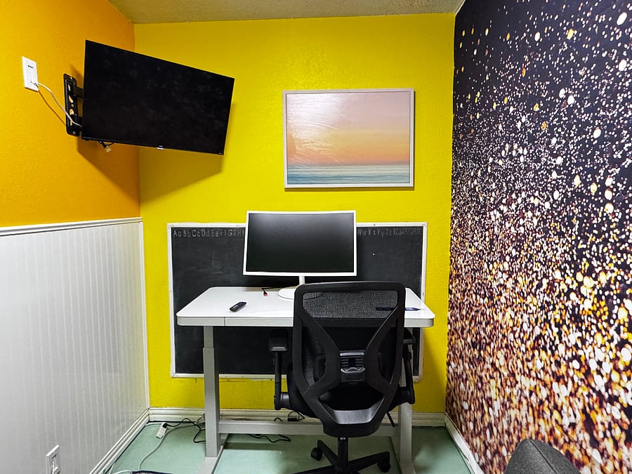 Private office with 27" curved monitor, smart TV, couch, and electronically adjustable desk for sitting or standing.