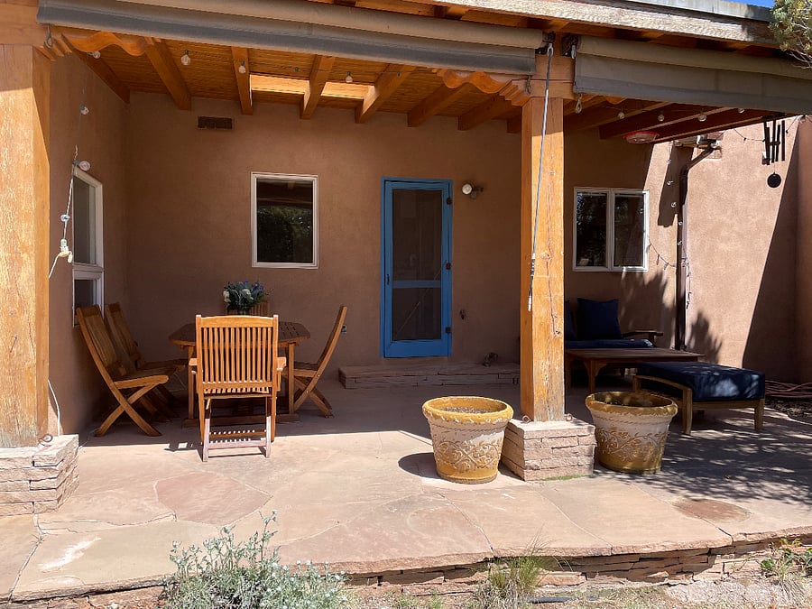 Outdoor dining and seating area under portal with roll-down shades. Gas grill is adjacent.