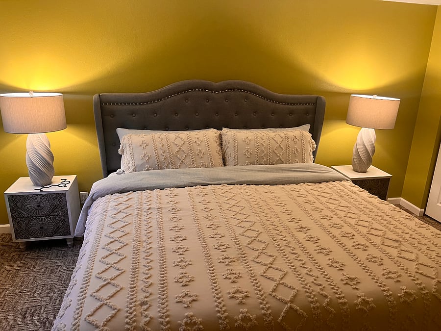 This cozy master bedroom exudes warmth and comfort King size bed. The space features a plush, textured bedspread. Soft lighting from elegant lamps on bedside tables enhancing the room tranquility.