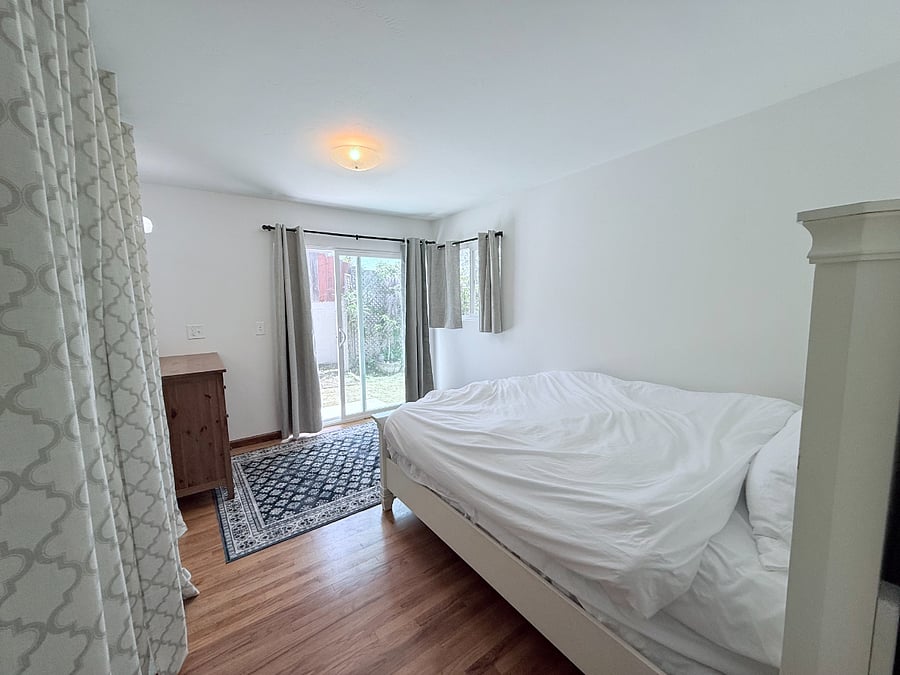 Queen bed in room with sliding door to spacious and fenced yard.