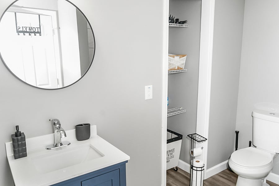 Contemporary bathroom with a bold navy vanity, round mirror, and open linen closet for easy access to towels and toiletries.