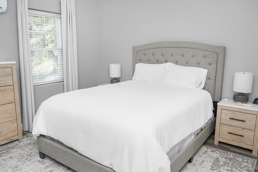 Relax in this calm and cozy bedroom featuring a tufted headboard, soft bedding, and lots of natural light.