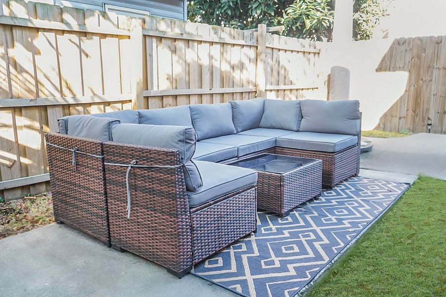 Relax outdoors with this cozy patio setup featuring a cushioned sectional, coffee table, and privacy fencing.