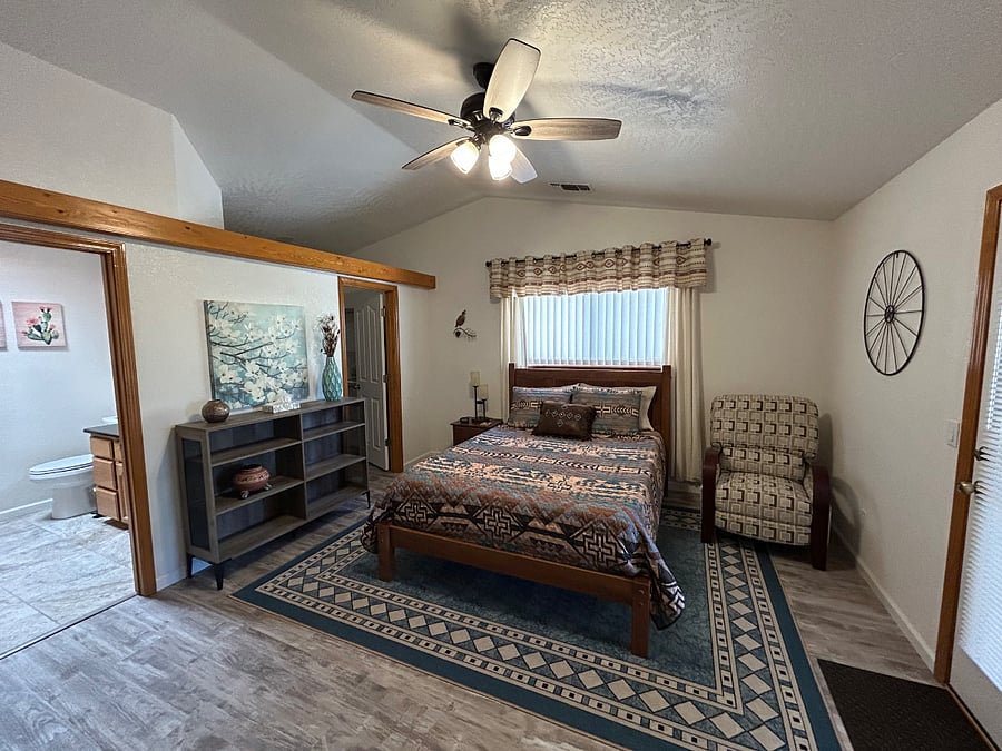 The bedroom suite is at the back of the house. It has a queen bed, walk-in closet, recliner, TV atop the bureau, desk, bookcase, and exterior door to the back patio.