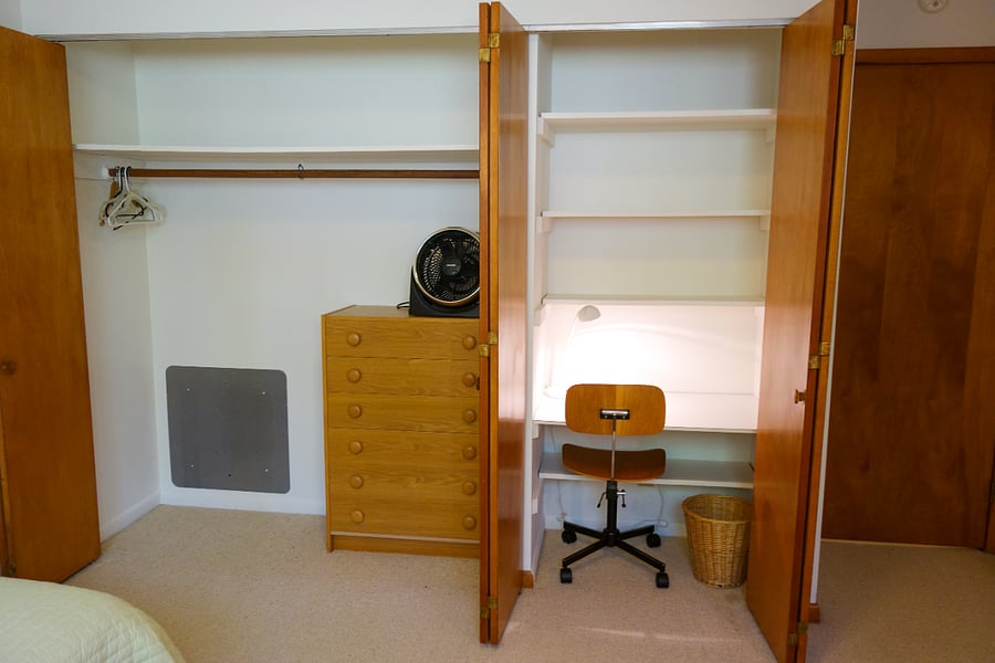 With the closet doors open, you can see there is plenty of storage space, a dresser, a fan, and a built in desk.