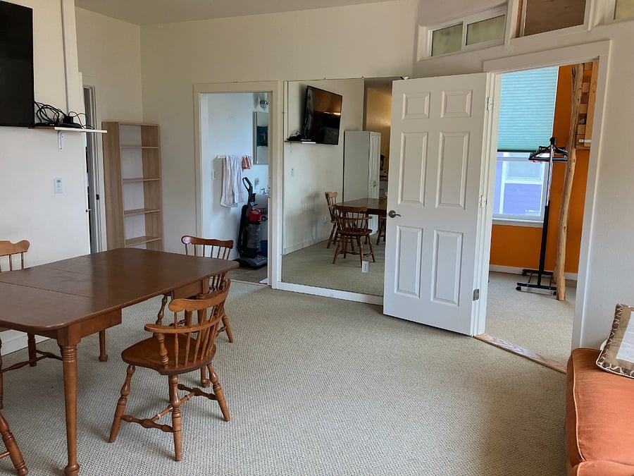 Large living/dining area has dining table, bookcase, wall storage for coats and shoes, sofa, and TV/sound system.