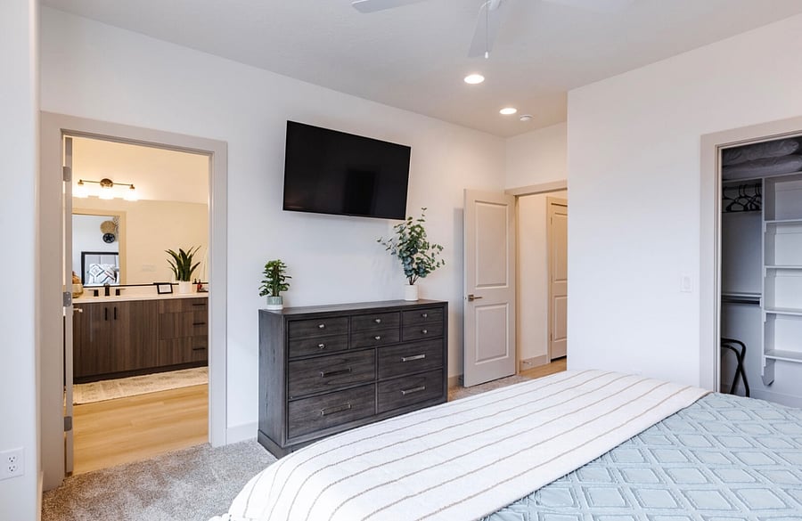 Primary bedroom with dresser, smart TV walk-in closet and view of en-suite bathroom.