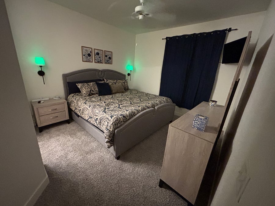 Primary bedroom with king bed, mounted smart tv, blackout curtains, noise machine, ceiling fan and remote control lights.