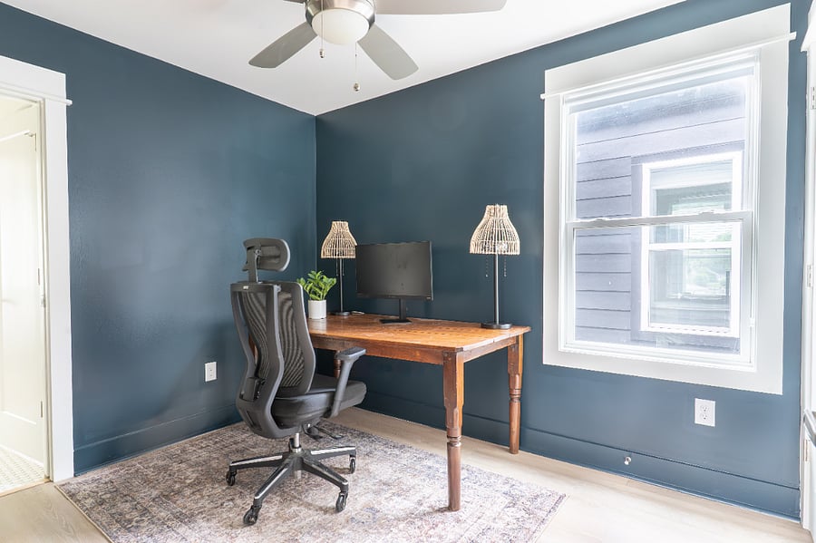 Upstairs office equipped with large desk, office chair, monitor, and background for video conferencing
