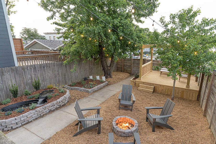 Fenced backyard with seating area, pond, and fire pit. Somewhat private from the neighbors thanks to the trees but still visible on either side