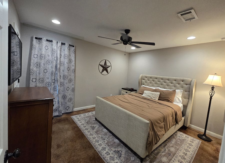 The warm and cozy primary bedroom features plush pillows, soft sheets, room-darkening curtains, and a TV.