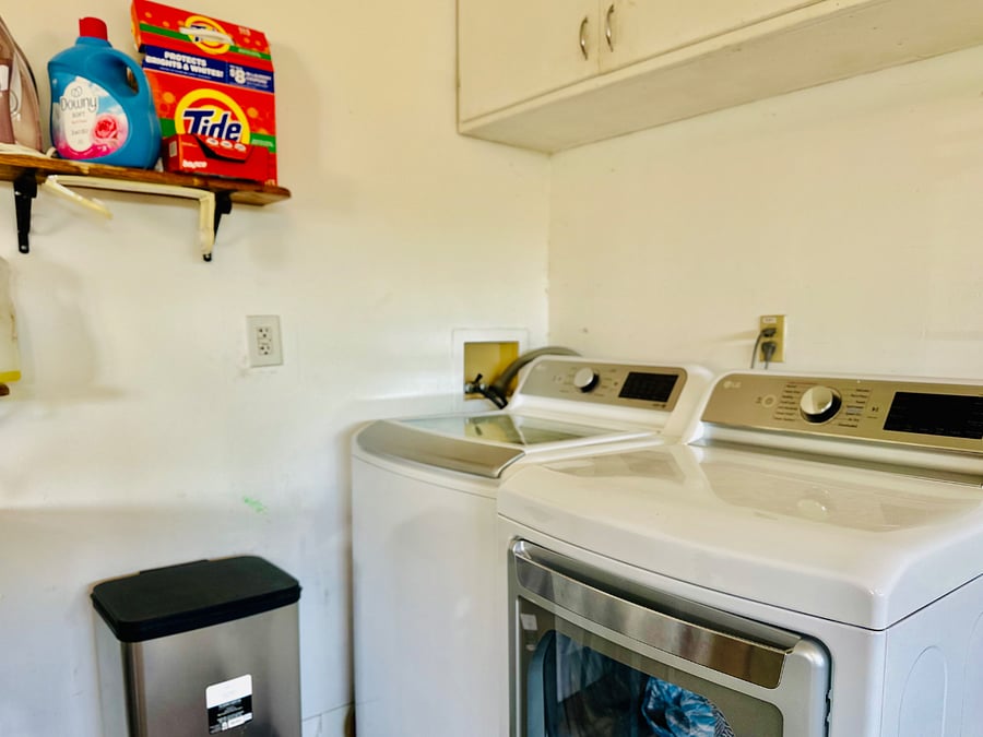 New washer and dryers in the garage along with a utility sink, trash bin, and extra storage.