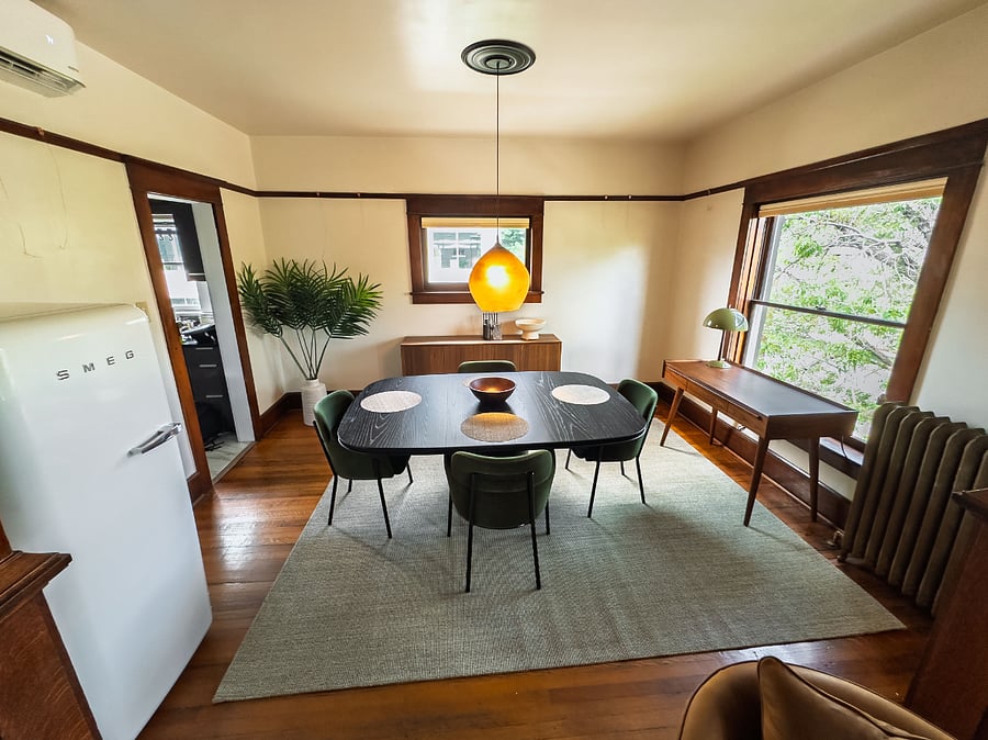 Chic dining room with green chairs gathered around a sculptural square table with a dedicated workspace and designer refrigerator.