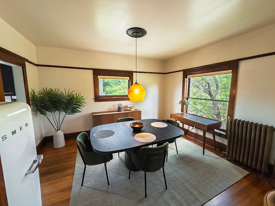 Chic dining room with green chairs gathered around a sculptural square table with a dedicated workspace and designer refrigerator.