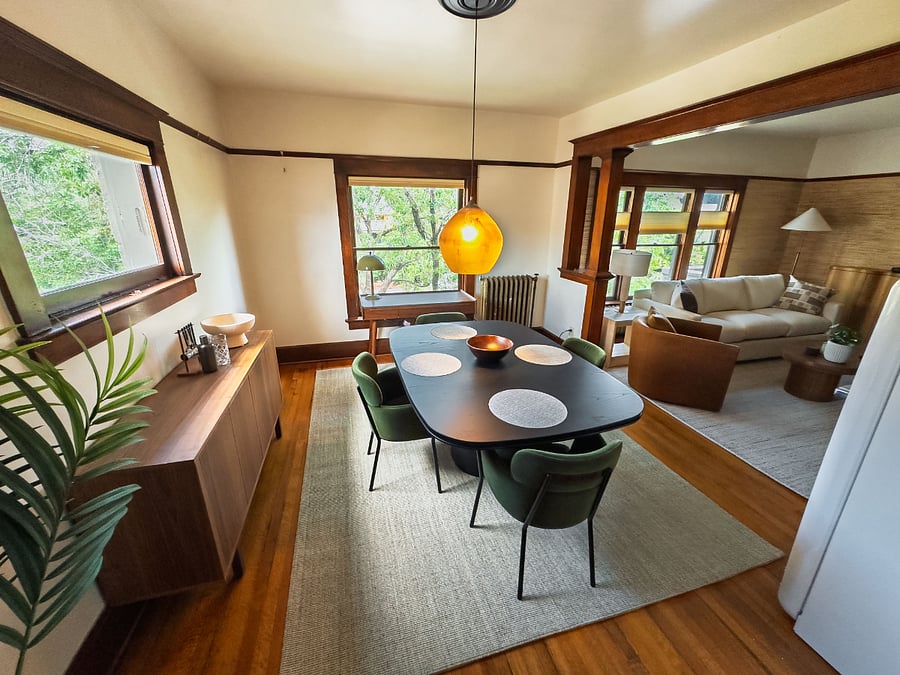 Chic dining room with green chairs gathered around a sculptural square table with a dedicated workspace and designer refrigerator.