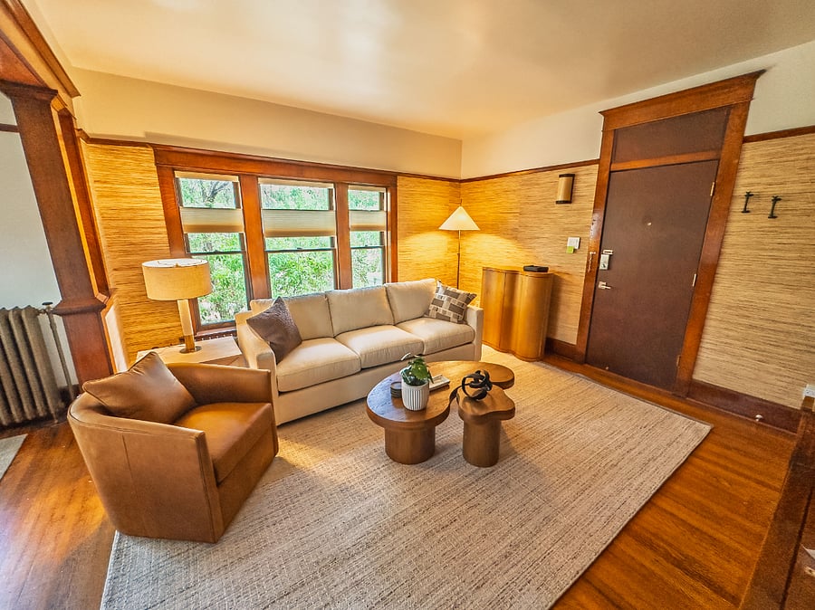 The elevated living room with warm, cherry hardwood details, city and mountain views, plenty of natural light, and lots of seating clustered around organic wood coffee tables.