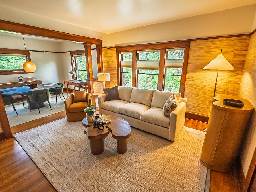 The elevated living room with warm, cherry hardwood details, city and mountain views, plenty of natural light, and lots of seating clustered around organic wood coffee tables.