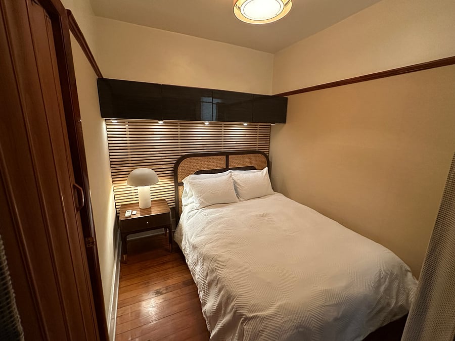 The cozy queen bedroom with a cane headboard, slatted wood accent wall, and mid-century nightstand with mushroom lamp.