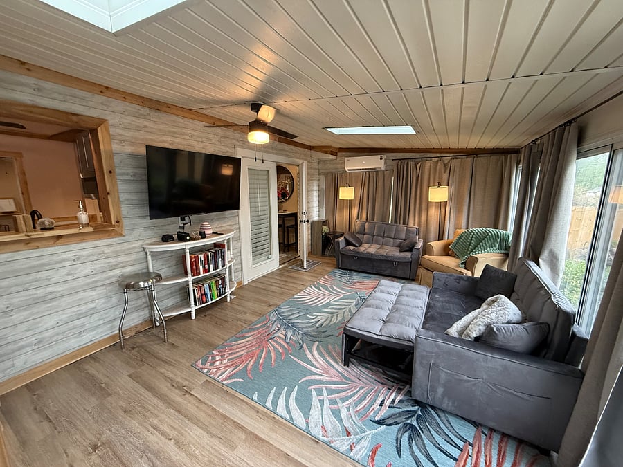 Sunroom with Smart TV and Passthrough from kitchen, 2 Sofa Sleepers and Glass windows look out to the large stone patio.