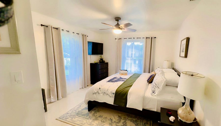 This large private bedroom includes a Casper Snow king-size mattress, quality Macys linens, Smart TV, blackout curtains, and ceiling fan ideal for travel nurses or professionals looking to rest well. The attached bathroom features a vanity, a shower, and a mirrored medicine cabinet, plus towel shelving. A wide dresser, mirrored closet, and refurbished terrazzo floors complete the space. Quiet, private, and easy to maintain designed for extended stays and real comfort.