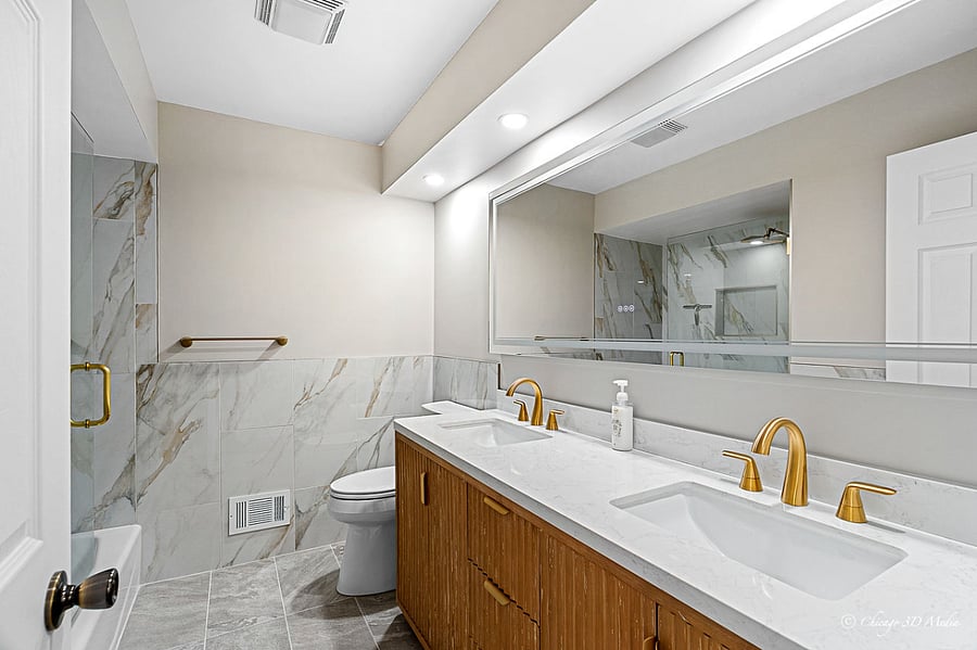 Luxurious Spa-like bathroom with gold fixtures, rain shower, and a double-sink vanity with large LED mirror w/defogger.