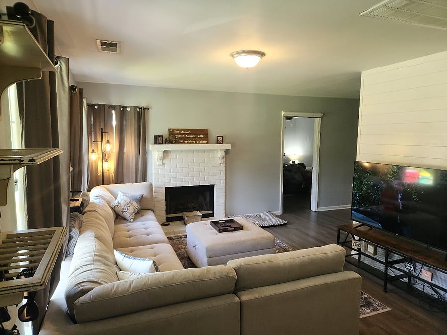 Cozy living room with large sectional couch, black out blinds, ceiling fan (added after this photo was taken) and a 55" Smart tv. Open flow to kitchen and additional seating area. Ceiling fan in place.