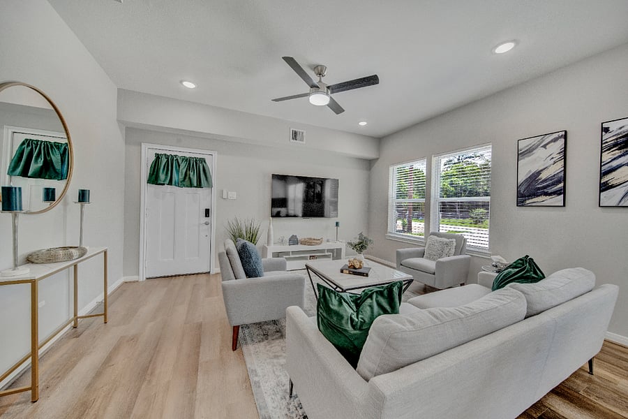 Haywood House features a modern, well-lit living room with a minimalist design. The room features light-colored walls and wooden flooring, creating a bright and airy atmosphere. Large windows on one side of the room allow natural light to flood in.