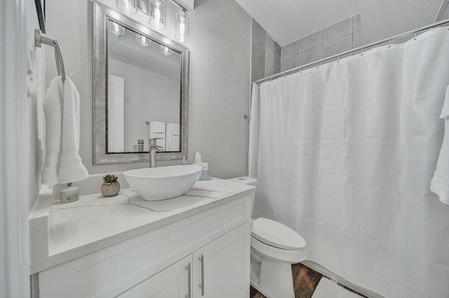 The hall bath is elegantly draped in white to give a clean, fresh look. Under the sink you will find a first-aid kit, hair dryer, and many essential items.