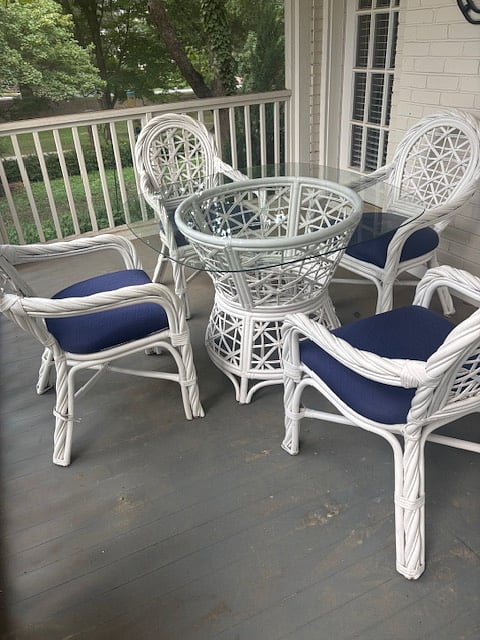 Screened in porch with a table and white wicker furniture overlooking the park. This is one of several outdoor seating areas.