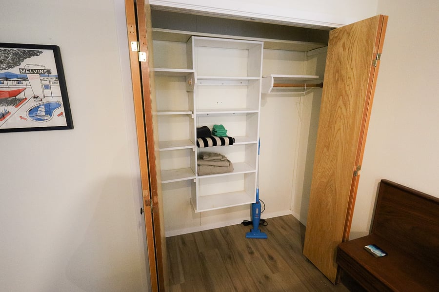 Accordion door closet next to the bed with extra linens and a vacuum.